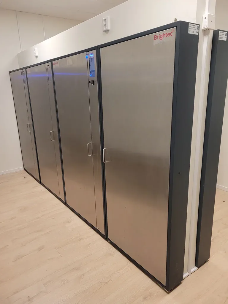 Fyra stora digitala nyckelskåp i rostfritt stål installerade i en vit lokal med trägolv.